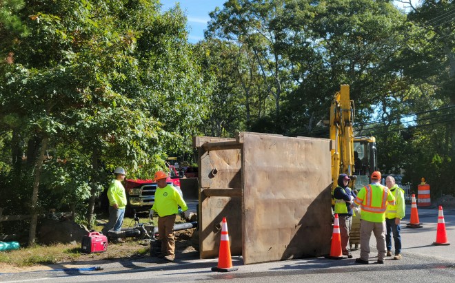 Construction workers gathered around a trench box by the side of the road