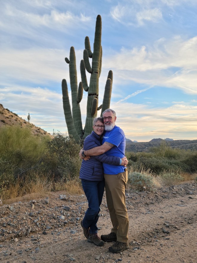 Man and woman embracing in front of a saguaro cactus at sunset