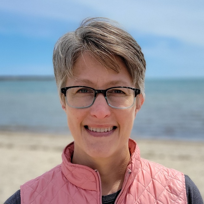 Lauri Hawley smiling at the beach, wearing a pink vest and blue eyeglasses